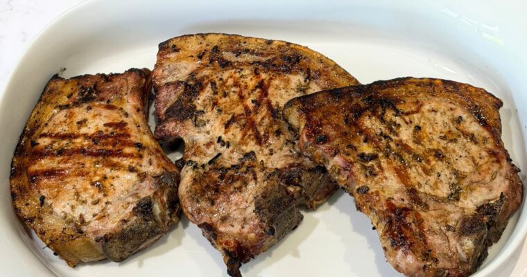Three cooked pork chops having been covered in truly yummy marinade and cooked on the BBQ presented in a white shallow dish.