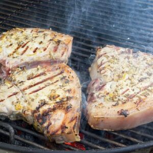 Three pork chops covered in marinade sizzling on a bbq.