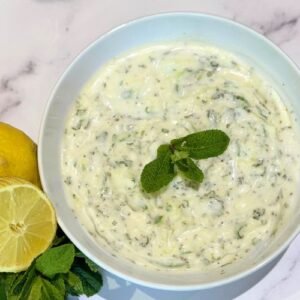 Close up shot of Truly Yummy Tzatziki in a bowl garnished with fresh mint and lemon on the side.