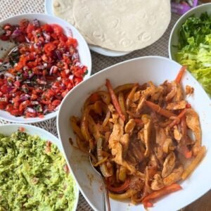 Several serving bowls with fajita fillings together with a pile of gluten free wraps.