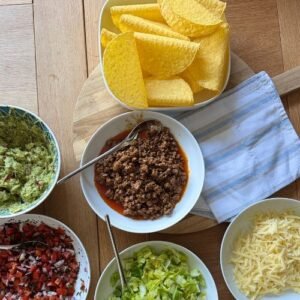 Selection of bowls filled with tacos, salsa, guacamole, cheese and shredded lettuce.